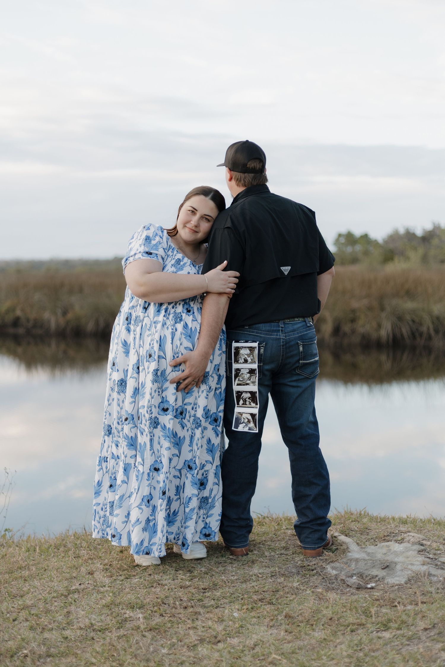 Emotional outdoor photoshoot by waterfront with couple sharing tender moment at sunset.