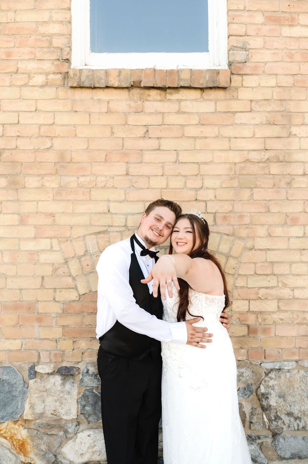A joyful wedding couple shares a romantic moment against a rustic brick wall backdrop.