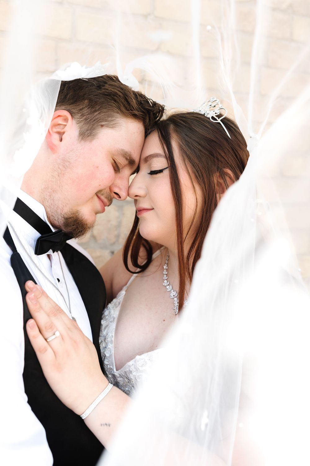 A romantic wedding portrait shows a couple embracing under a delicate white veil.