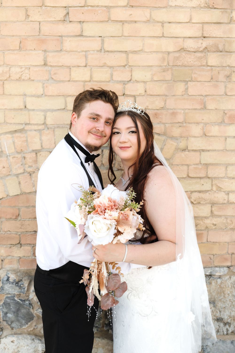 A couple in wedding attire poses for romantic photos against a vintage brick wall backdrop.