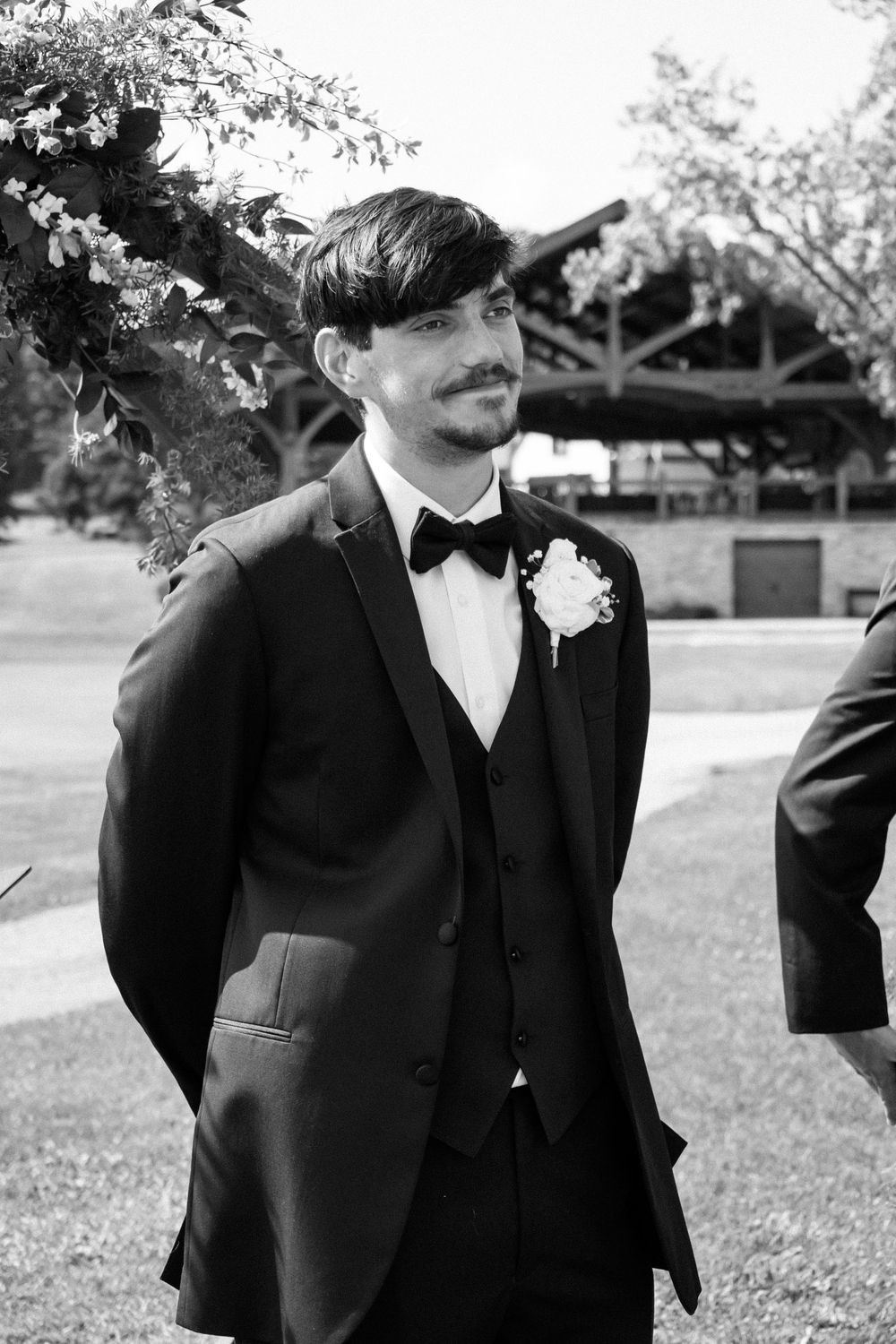 A group of groomsmen in black tuxedos and bow ties stand together outdoors during a formal wedding event.