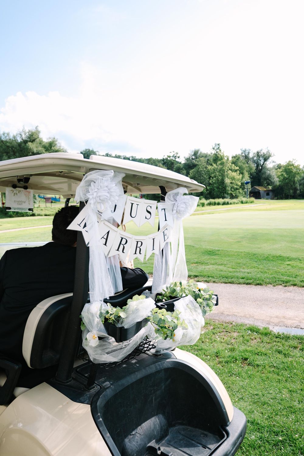 Golf cart decorated with 'Just Married' sign parked on grassy course for wedding celebration.