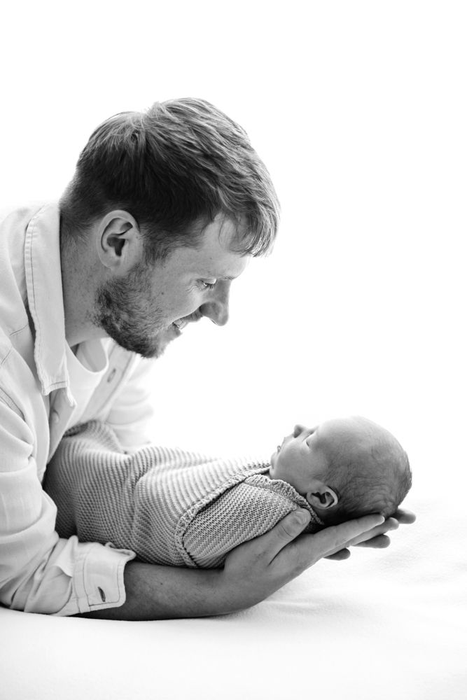A black and white portrait of a new dad cradling newborn baby holding them face to face.