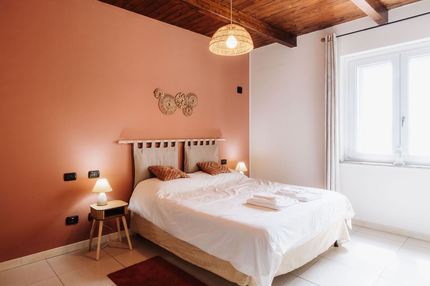 Modern minimalist bedroom interior with wooden ceiling beams, white bedding, and warm terracotta-colored walls.