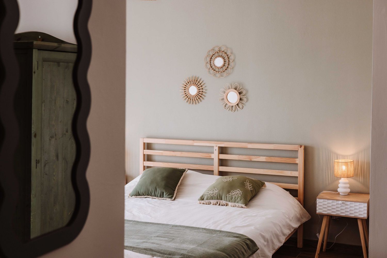 A modern bedroom with wooden furniture, white bedding, and wall decor featuring sunburst mirrors.