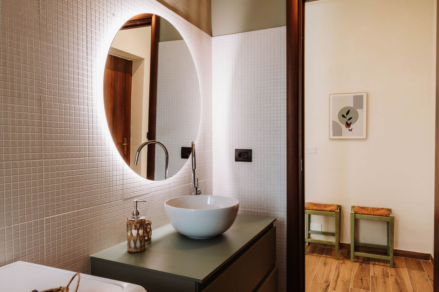 A modern bathroom interior with white tile walls, wooden accents, and a circular mirror above a sleek vanity.