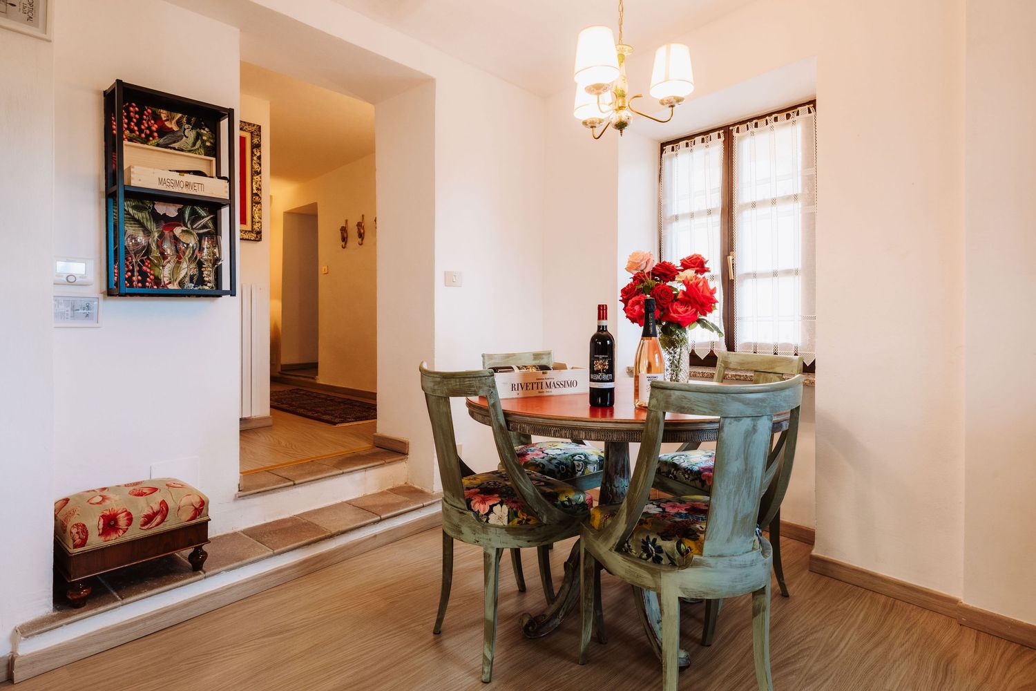 Cozy dining nook with mint green chairs, round table, wine bottle, and red floral centerpiece in sunlit corner.