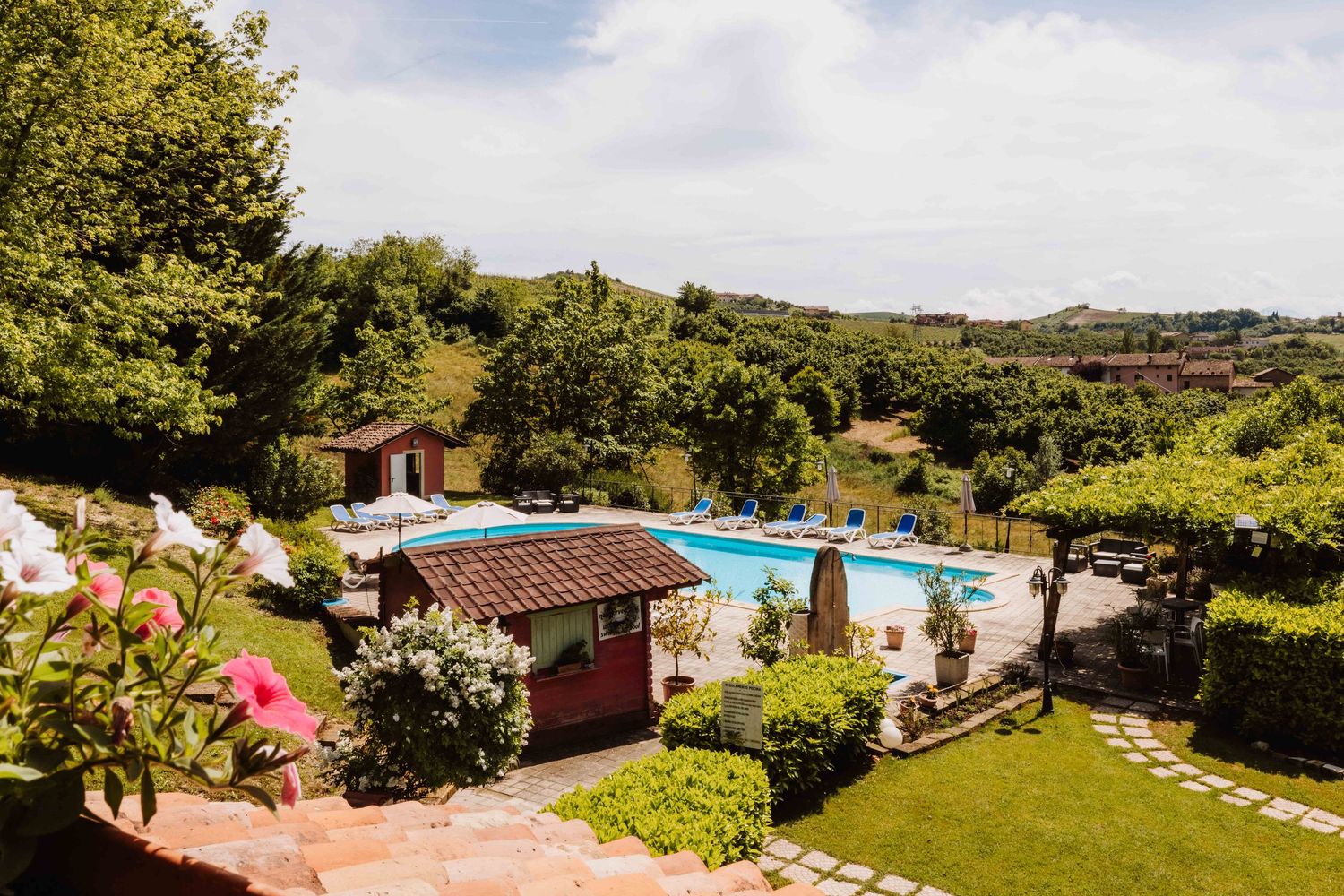 A panoramic view of a rustic Italian villa with a swimming pool surrounded by lush gardens and rolling hills.