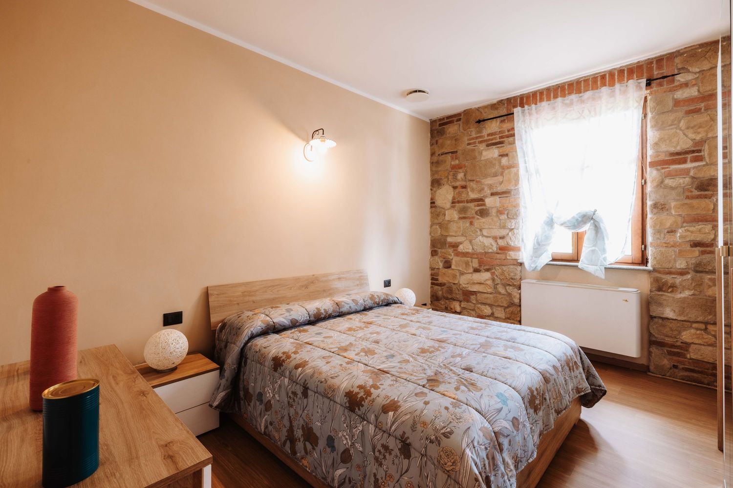 A modern bedroom with exposed brick walls features multiple beds and rustic decor in a panoramic view.