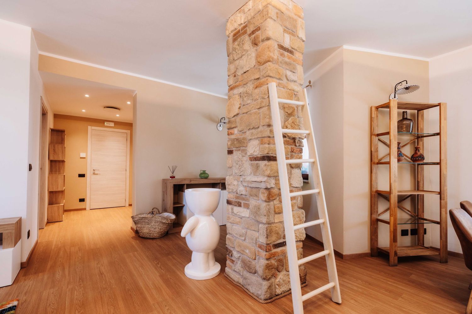 Modern basement hallway with white walls, stone accents, and wooden shelving units along one side.