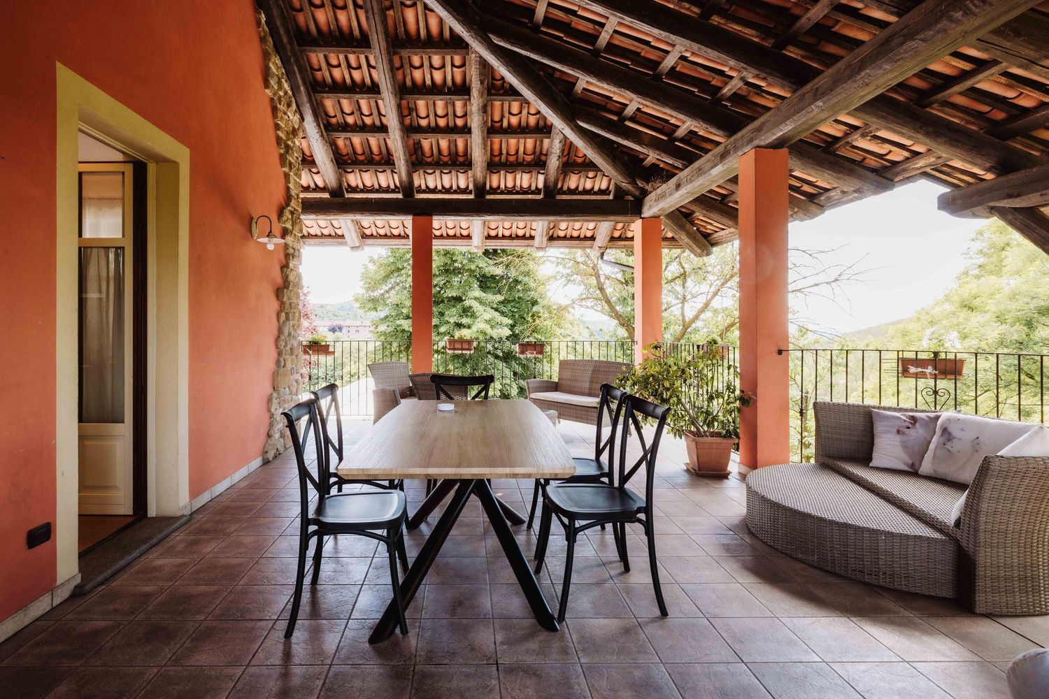 Rustic covered outdoor patio with wooden beams and stone columns overlooking a scenic mountain landscape.