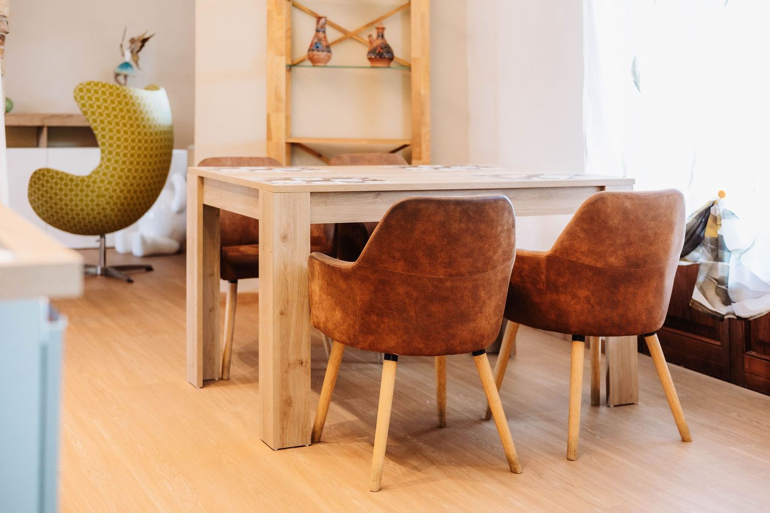 Modern dining room interior with brown leather chairs and wooden table in a bright minimalist setting.