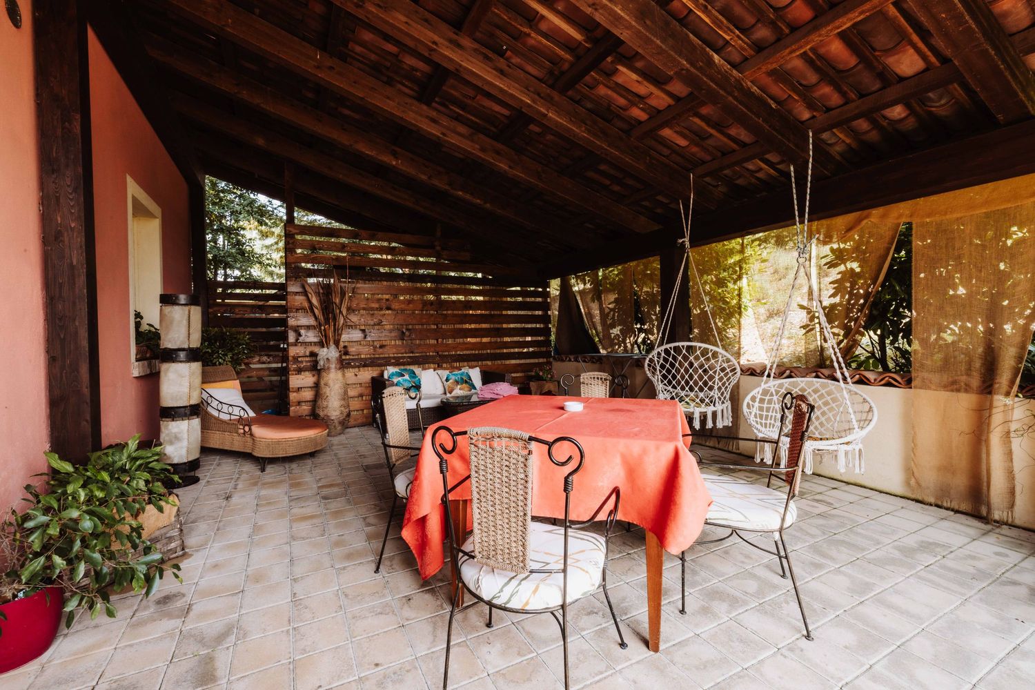 Cozy covered patio with rustic wooden ceiling, metal chairs, and coral tablecloth in outdoor dining area.