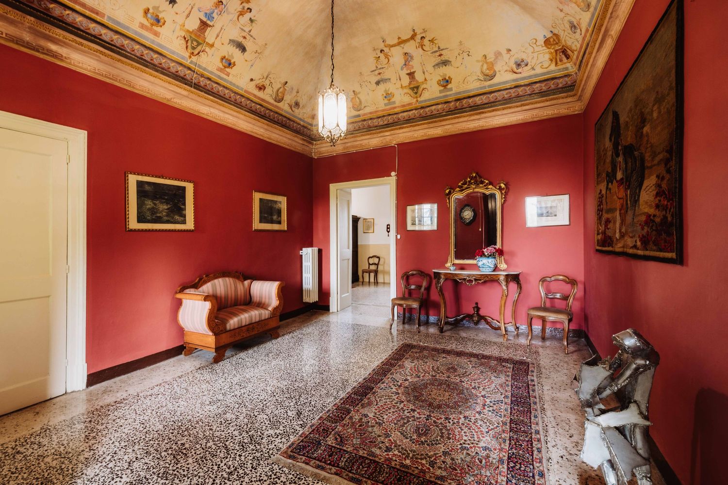 Elegant red room with ornate ceiling, antique furniture, and decorative Persian rug in a historic Italian villa.