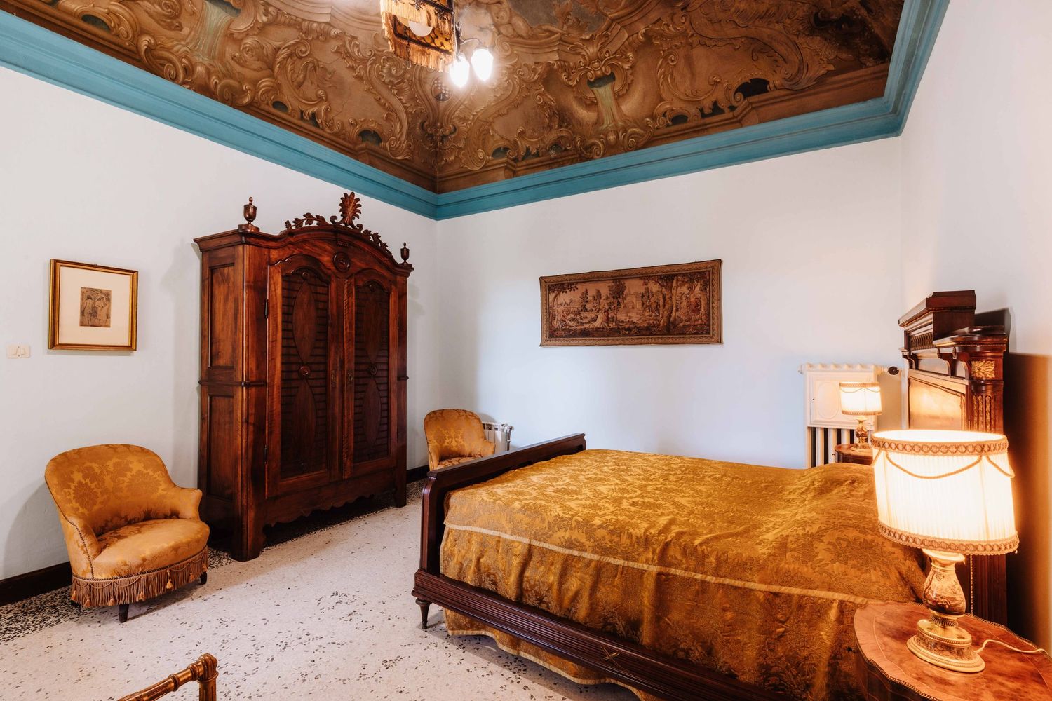 Elegant vintage bedroom with ornate ceiling, wooden armoire, golden bedspread, and turquoise trim details.