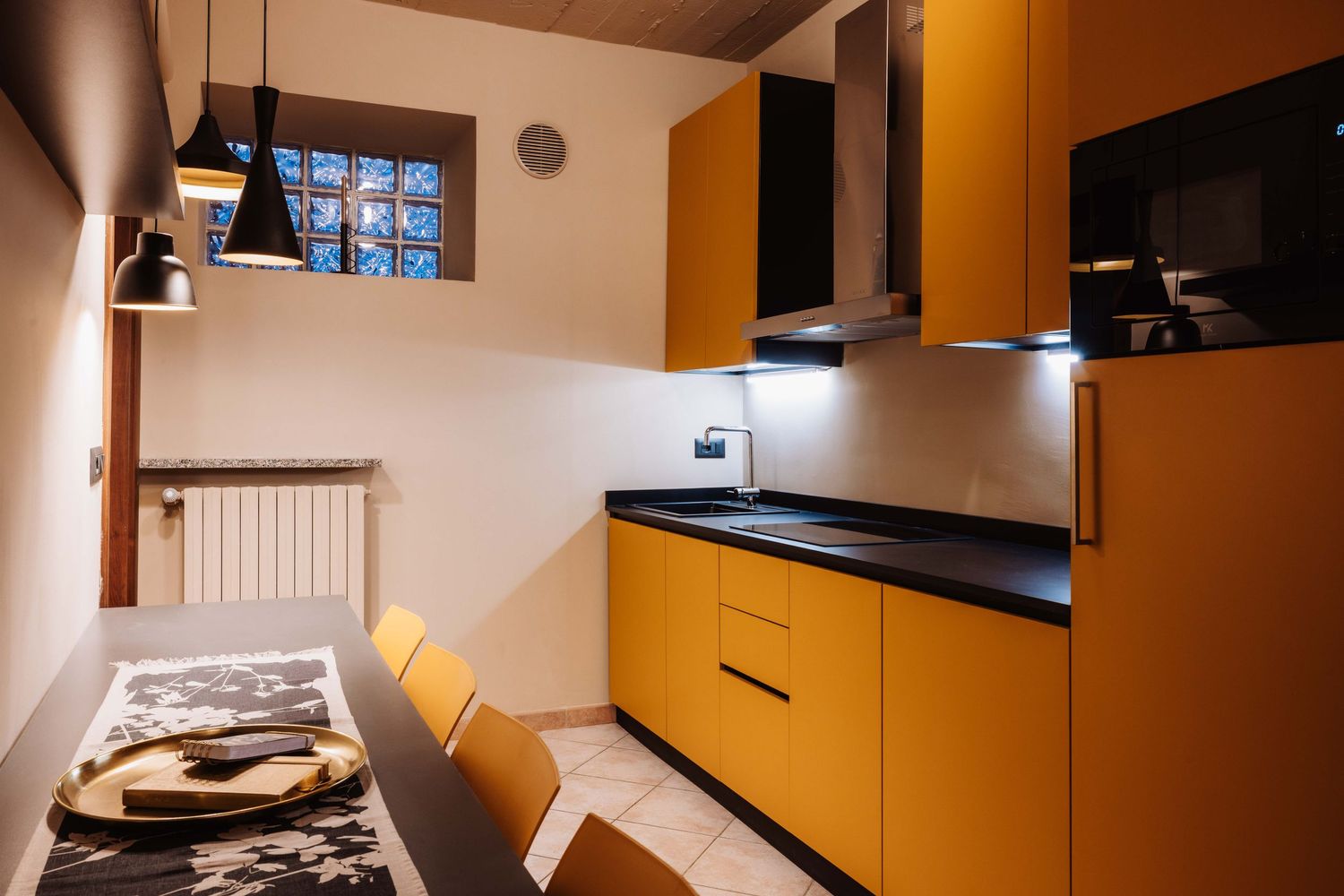 Modern kitchen interior with bright yellow cabinets, black countertop, and dining area with wooden chairs.