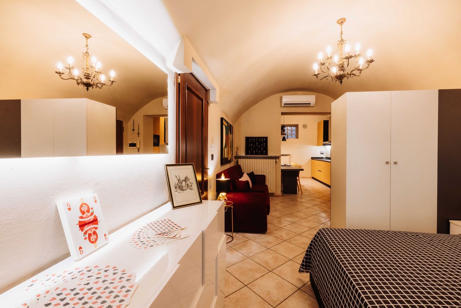 Modern studio apartment interior with arched ceiling, chandeliers, and tiled flooring in warm beige tones.