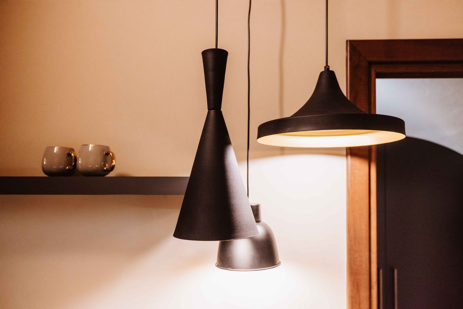 Modern black pendant lights hang elegantly over a wooden shelf with ceramic decor in a minimalist interior setting.