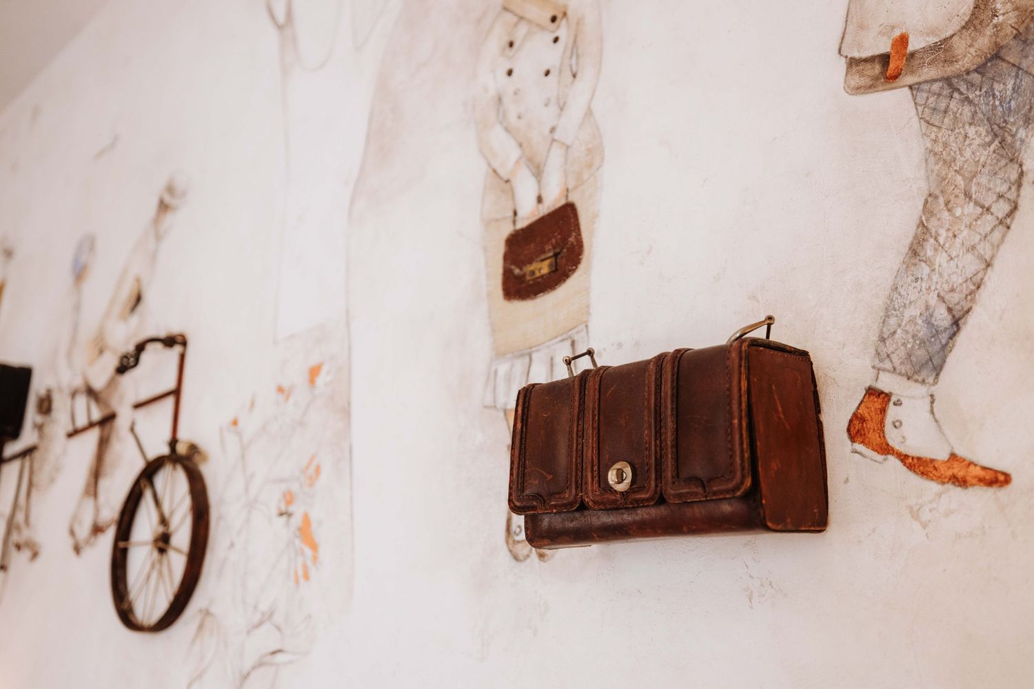Vintage brown leather purses and bags displayed on a white wall with decorative illustrations and sketches.