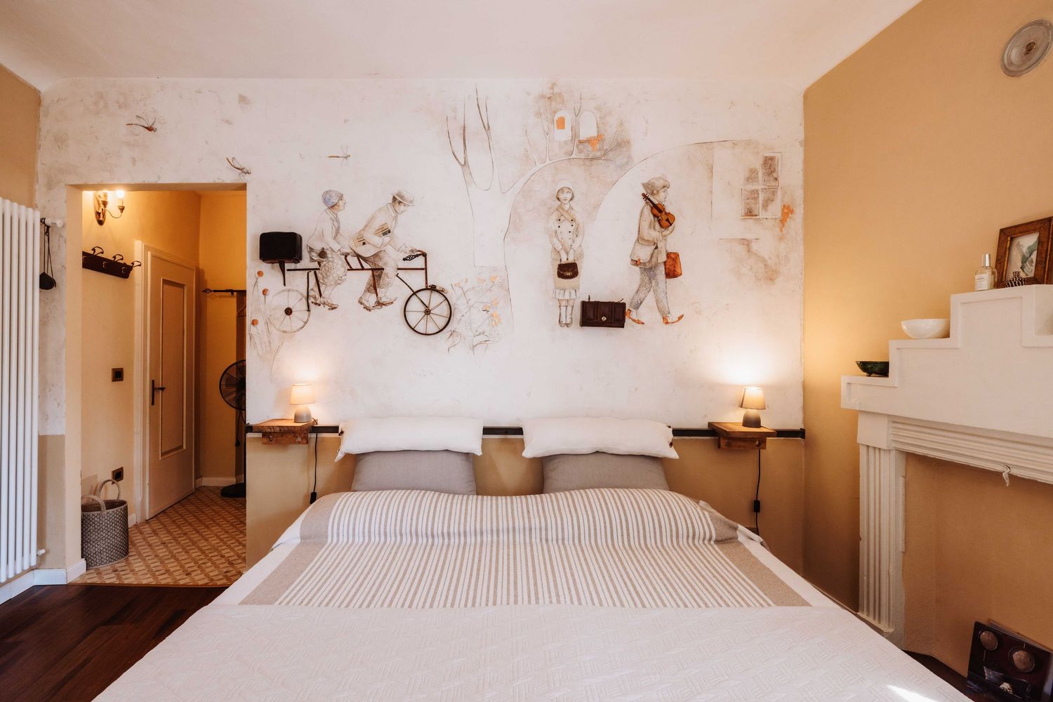 Modern bedroom with white bedding and artistic wall murals featuring whimsical designs and bicycle illustrations.