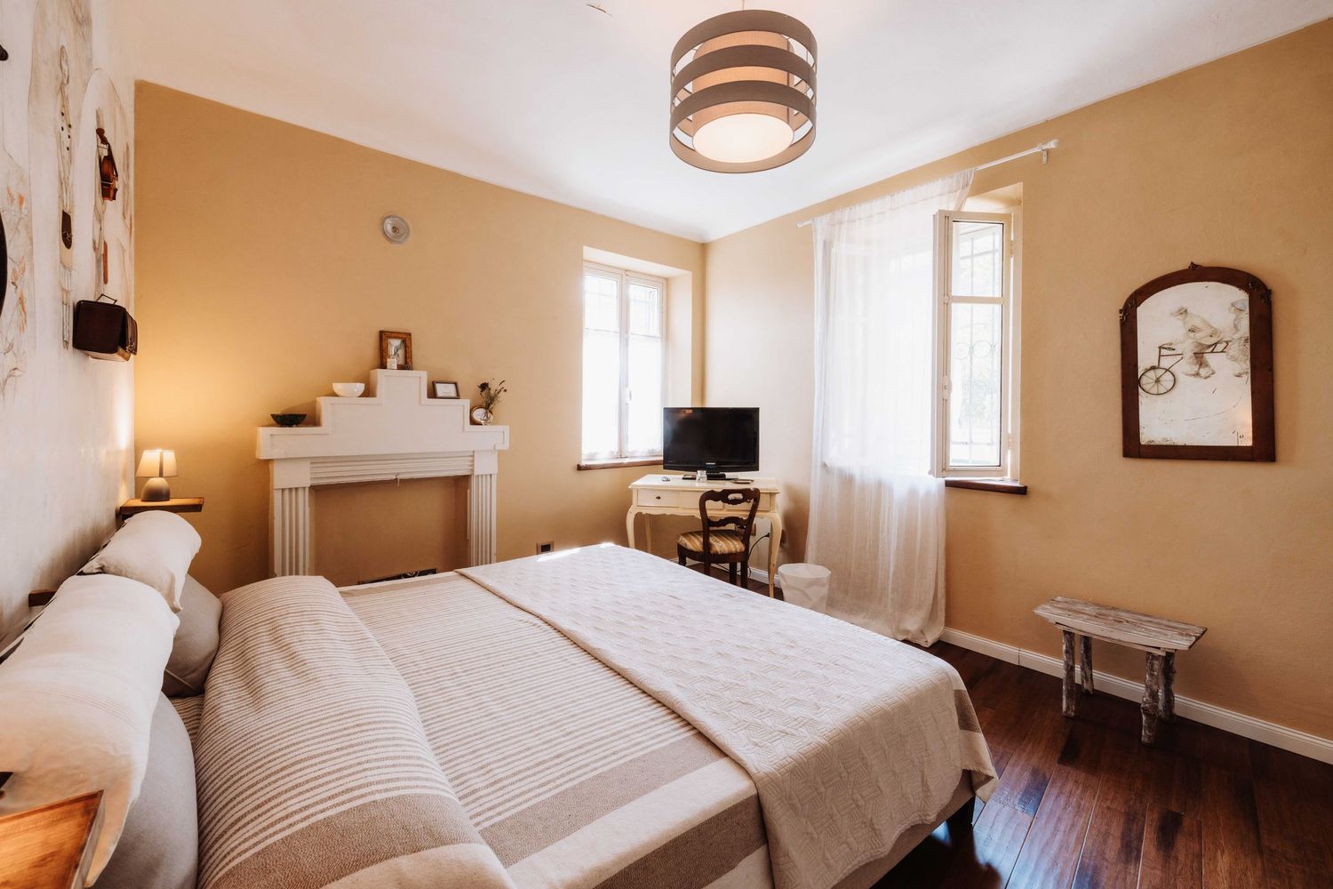 Panoramic view of a cozy bedroom interior with white bedding, beige walls, and natural light from multiple windows.