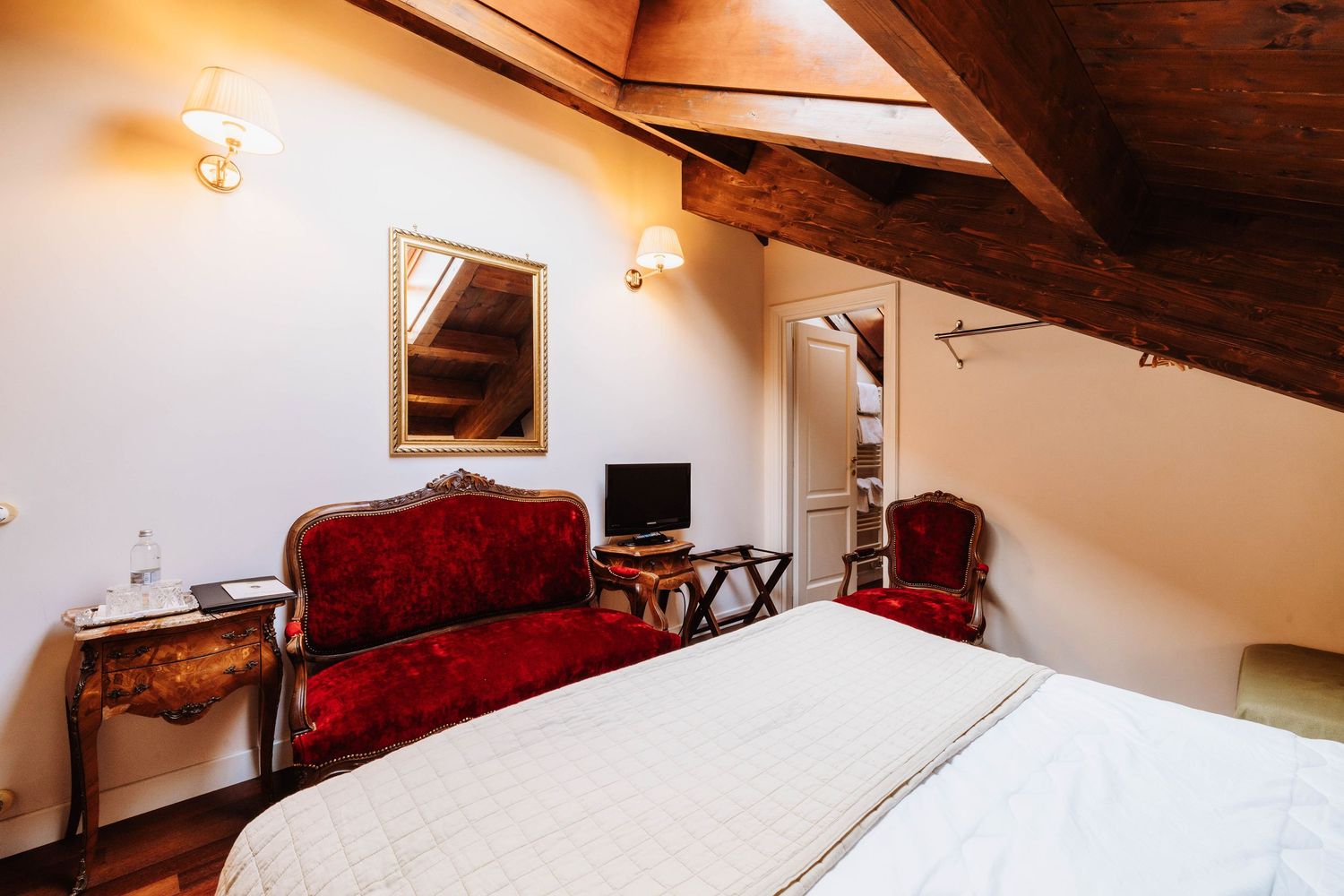 A cozy attic bedroom with sloped wooden ceiling, white bedding, and warm lighting creates an inviting atmosphere.