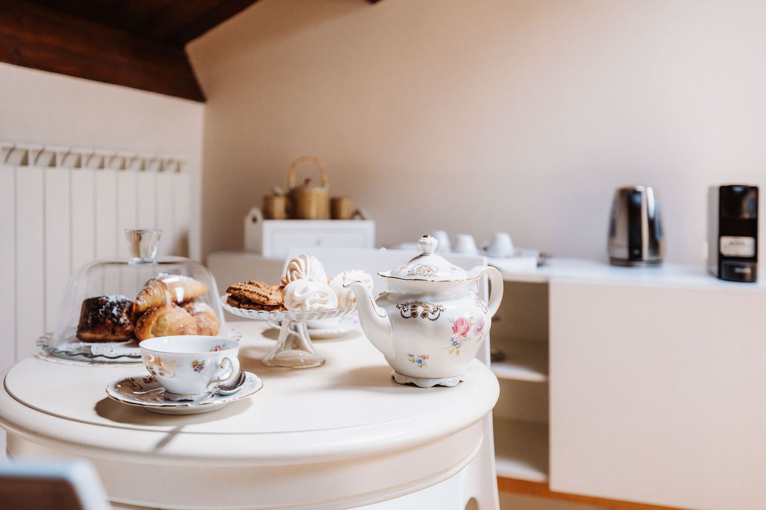 Elegant afternoon tea setup with white porcelain teacups and pastries on a round table in natural light.