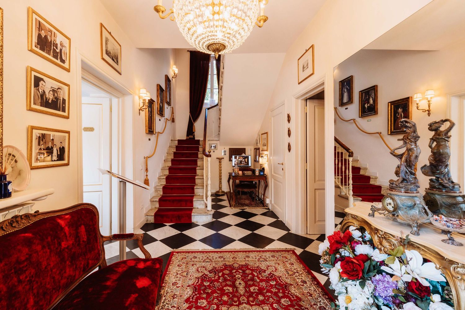 Elegant Victorian-style interior room with crystal chandelier, red carpet, and ornate antique furnishings.