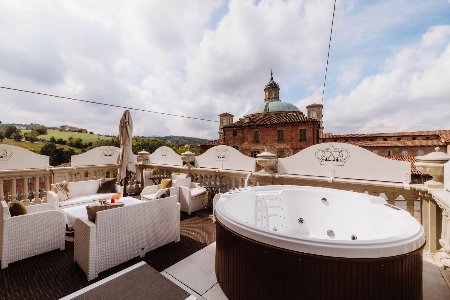 Rooftop hot tub and lounge area with white seating and historic brick building with clock tower in background.
