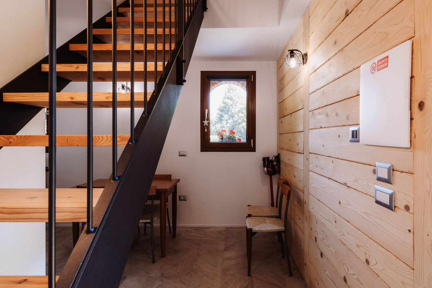 Modern wooden staircase with black metal railings leads upstairs in a bright minimalist home interior.