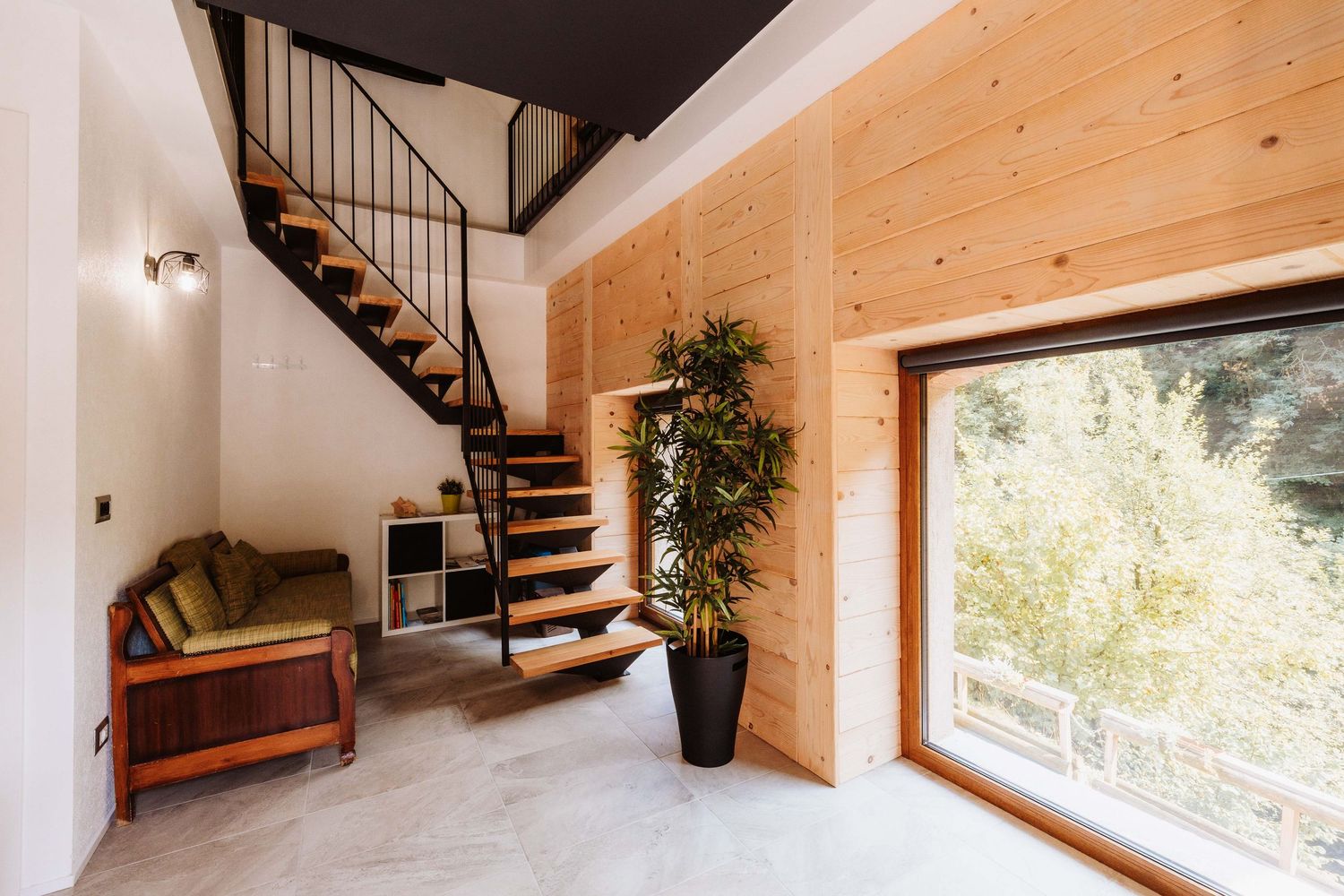 Modern wooden staircase with black metal railings leads upstairs in a bright minimalist interior with natural light.
