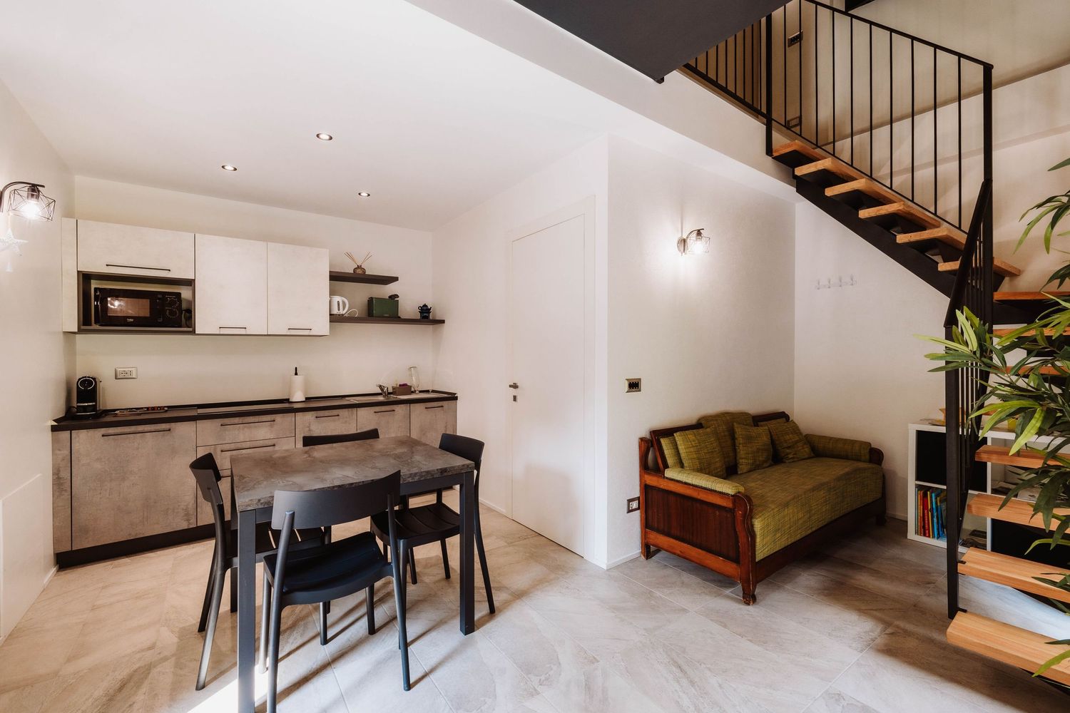 Modern open concept living room with wooden staircase, gray sofa, and minimalist decor in a bright interior space.