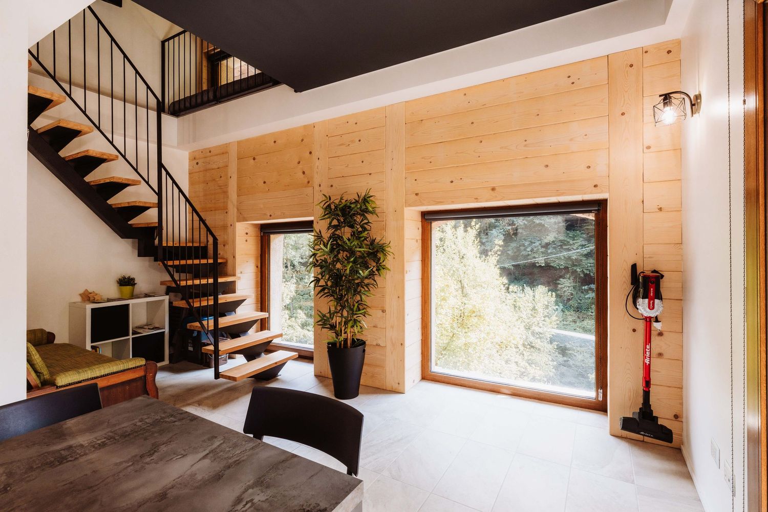 Modern wooden loft interior with exposed beams, spiral staircase, and natural light streaming through windows.