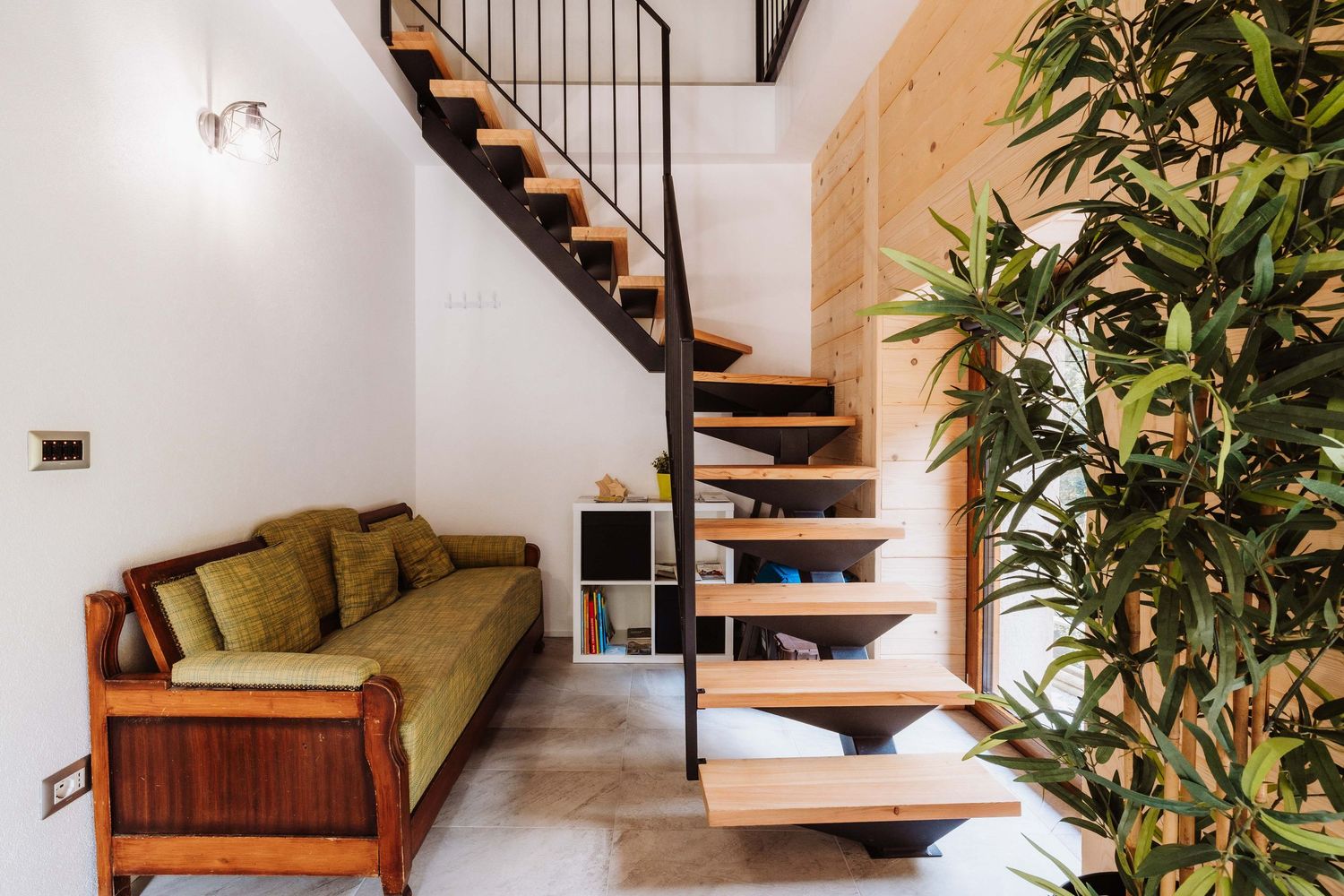 Modern wooden staircase with floating steps leads to upper level in minimalist home interior with potted plants.