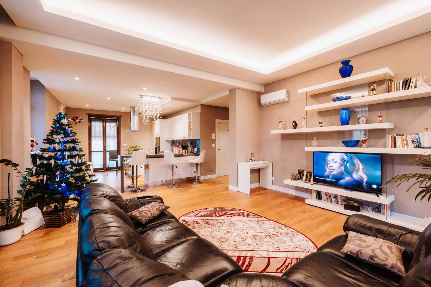Modern living room interior with recessed lighting, floating shelves, and a decorated Christmas tree in the corner.