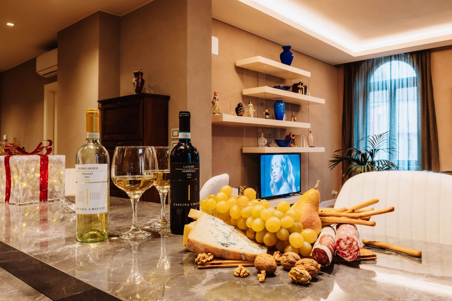 Elegant hotel room service display featuring wine glasses, fresh fruit, bread and charcuterie on a marble countertop.
