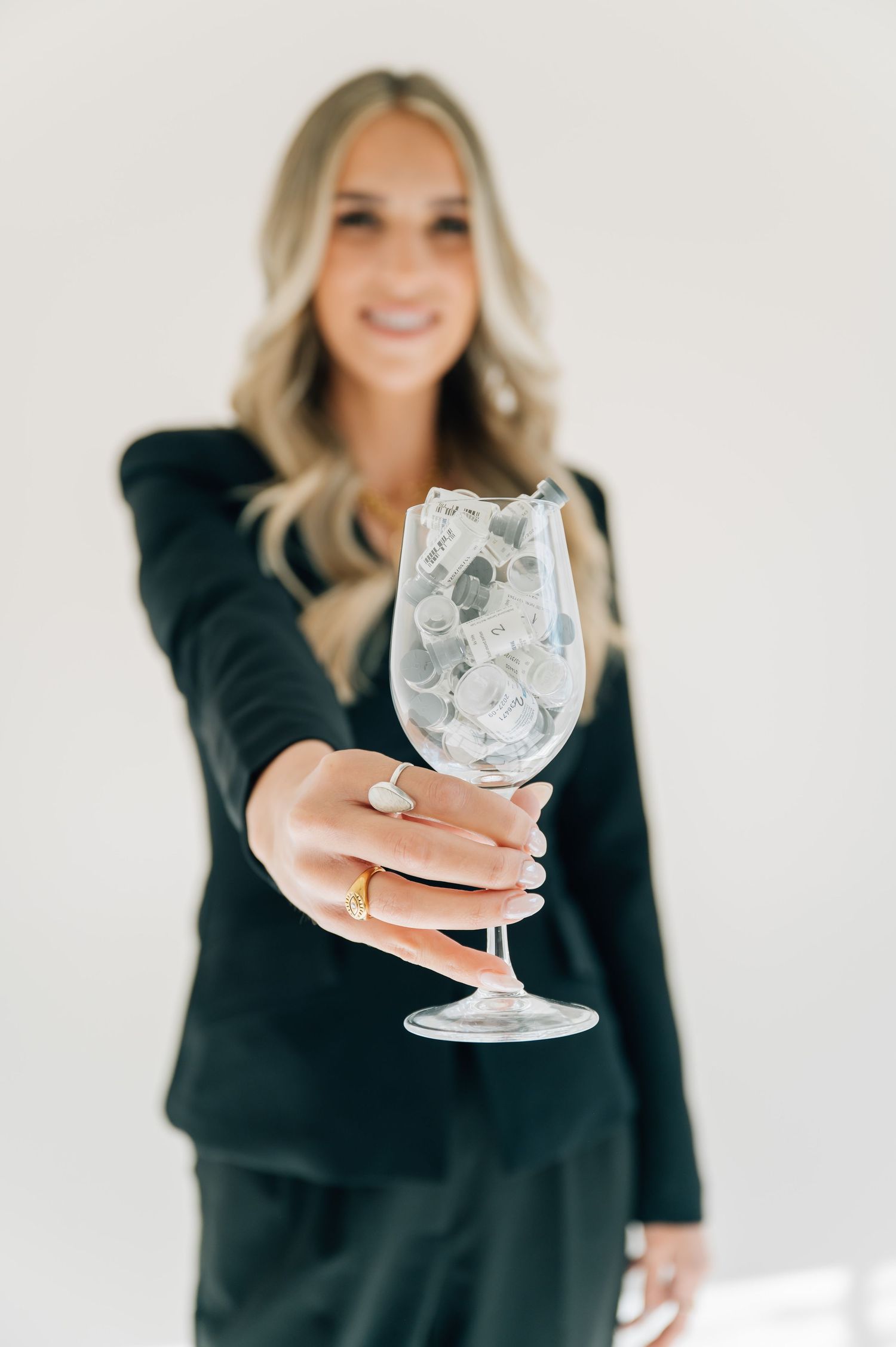Woman in black suit holding crystal wine glass against white background.