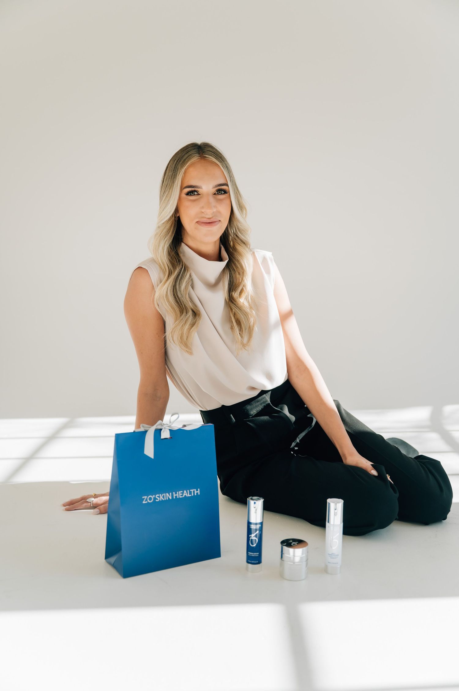 Professional lifestyle product photography with blue branded bag and skincare items on white background.