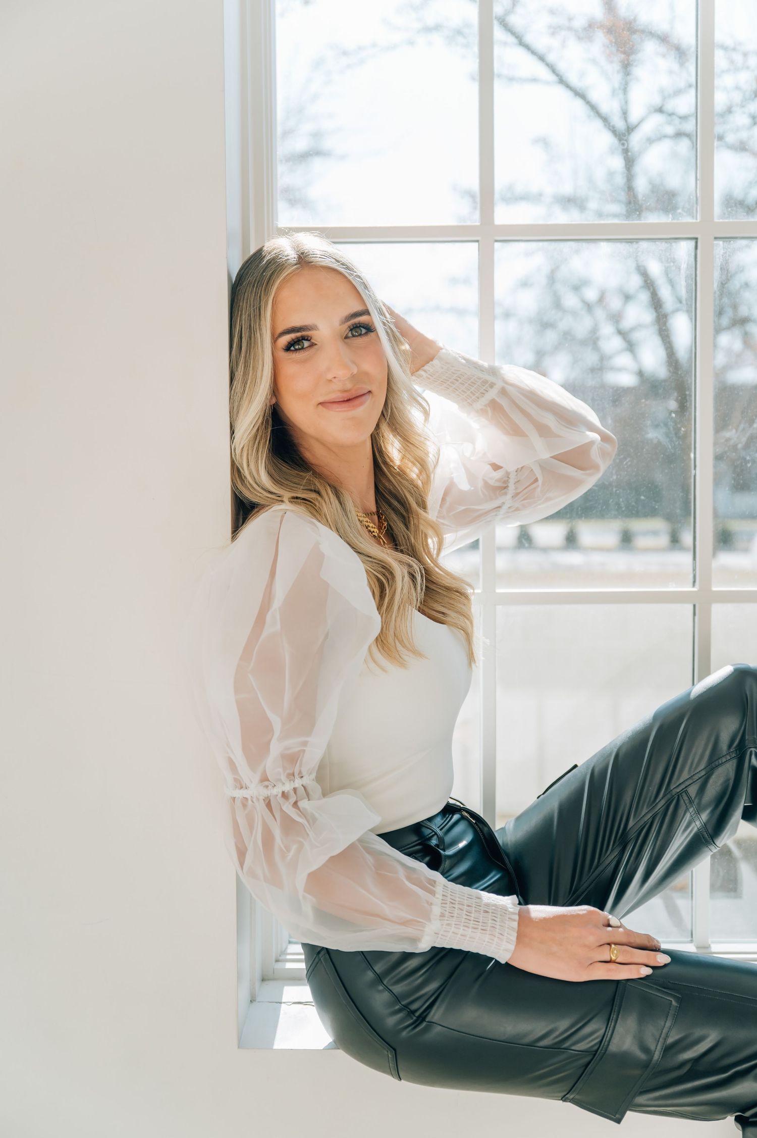 Lifestyle product photography in bright sunlit room with leather pants and white blouse.
