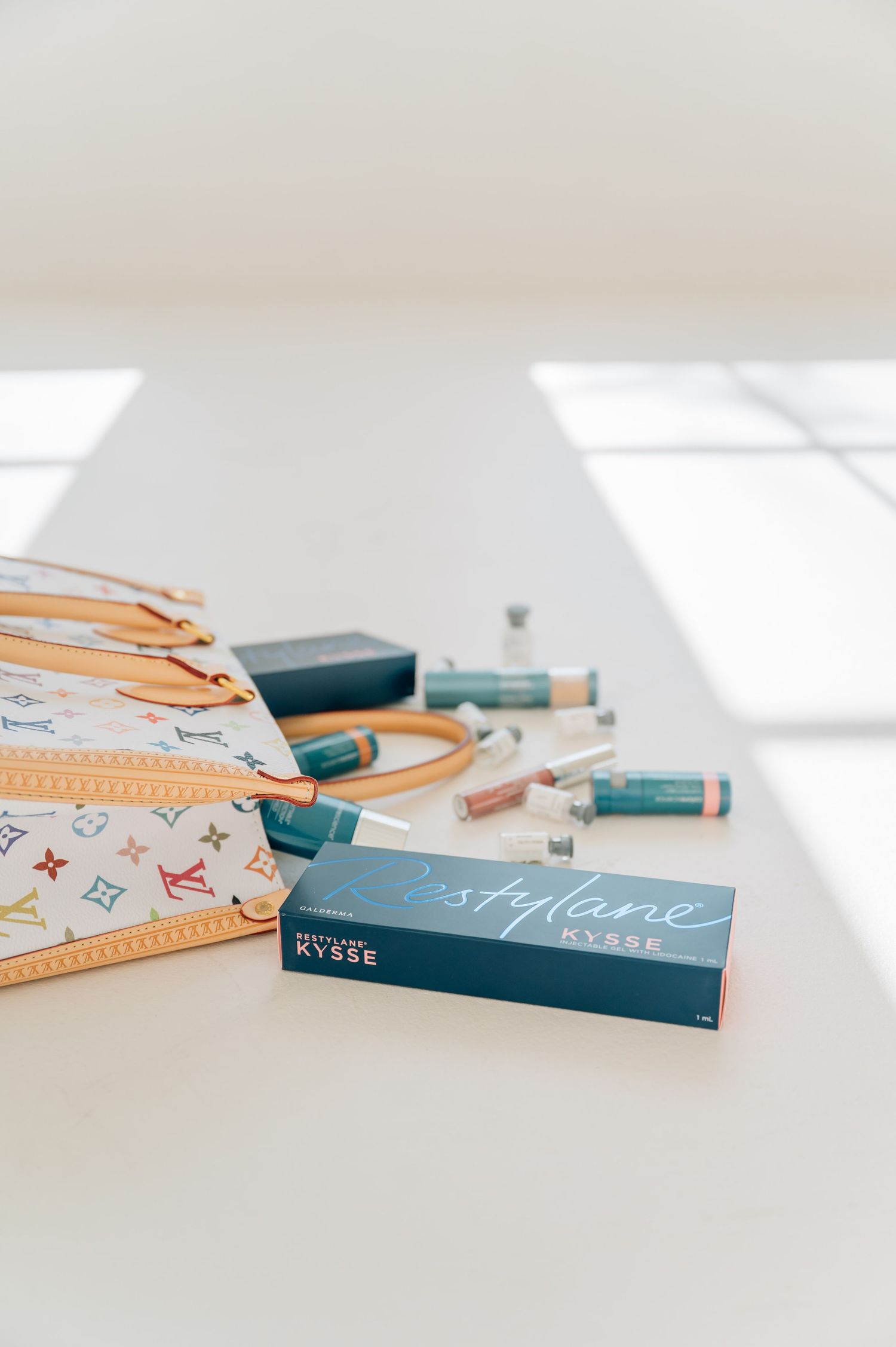 Minimalist flat lay of blue Kylie cosmetic products with orange ruler and designer pattern on white surface.