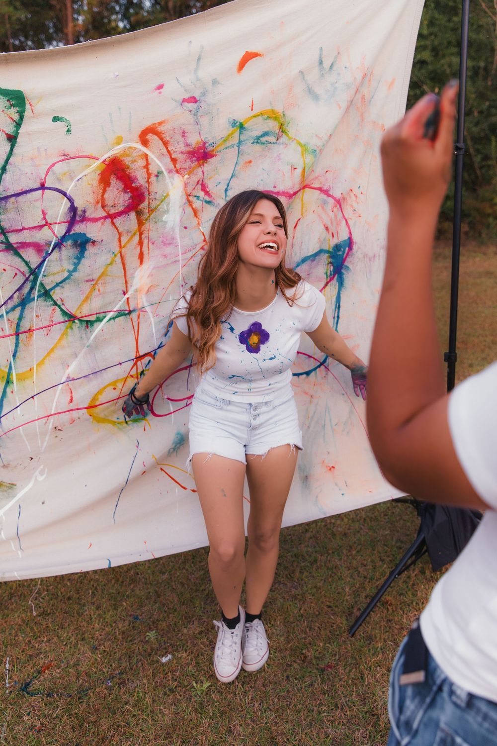 Colorful paint splatter art session outdoors with white canvas backdrop and joyful creative expression.