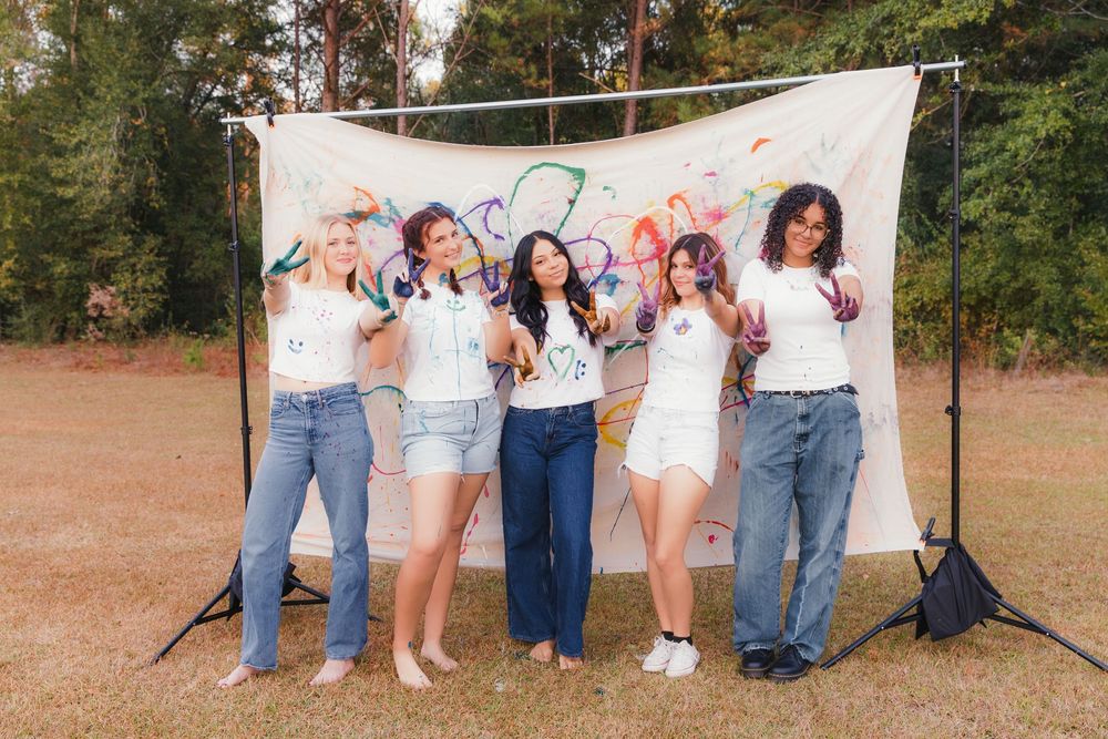 A group poses outdoors against a rustic backdrop wearing casual denim and white clothing for a coordinated photo shoot.