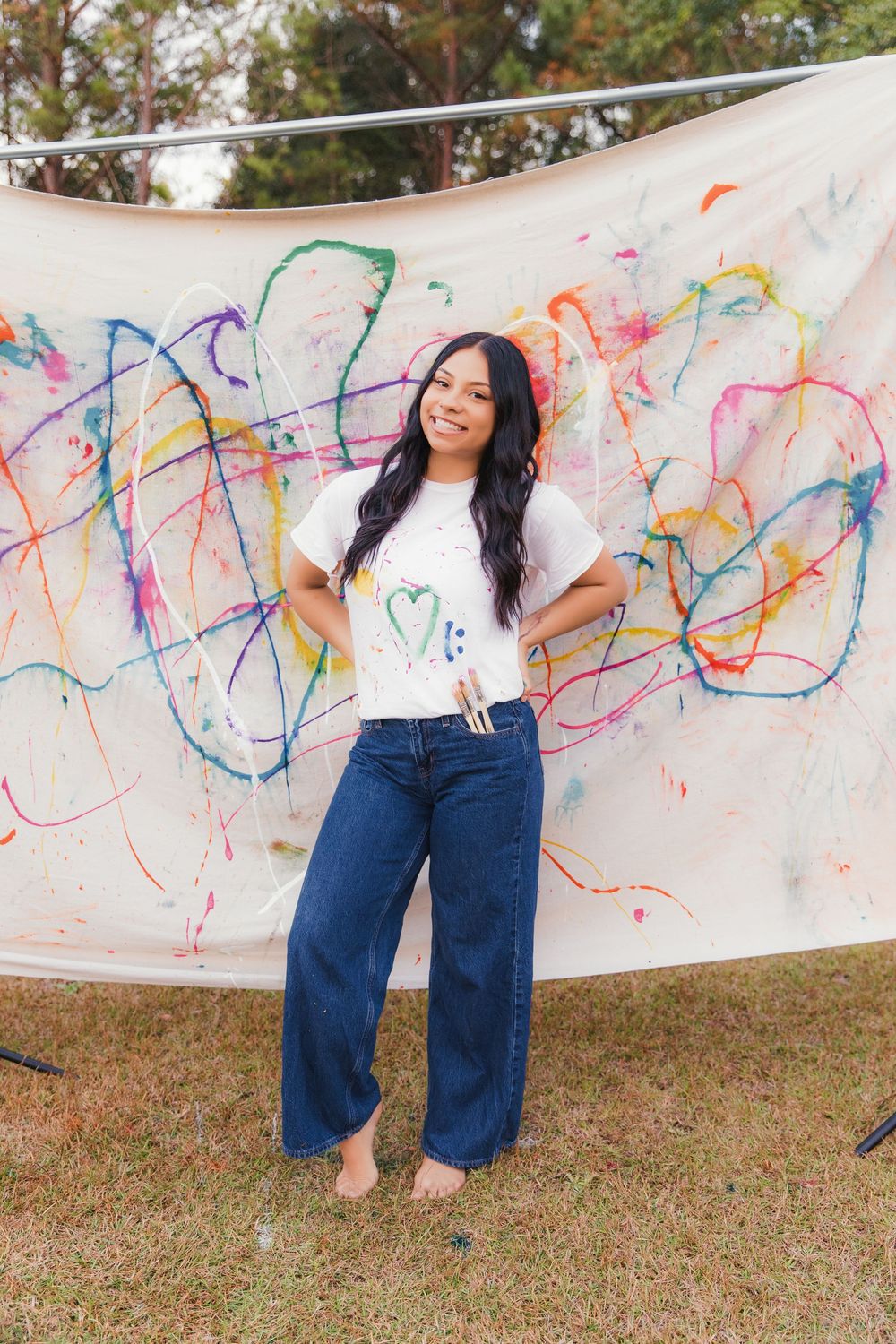 A series of photos showing someone in casual attire posing against a colorful paint-splattered backdrop outdoors.