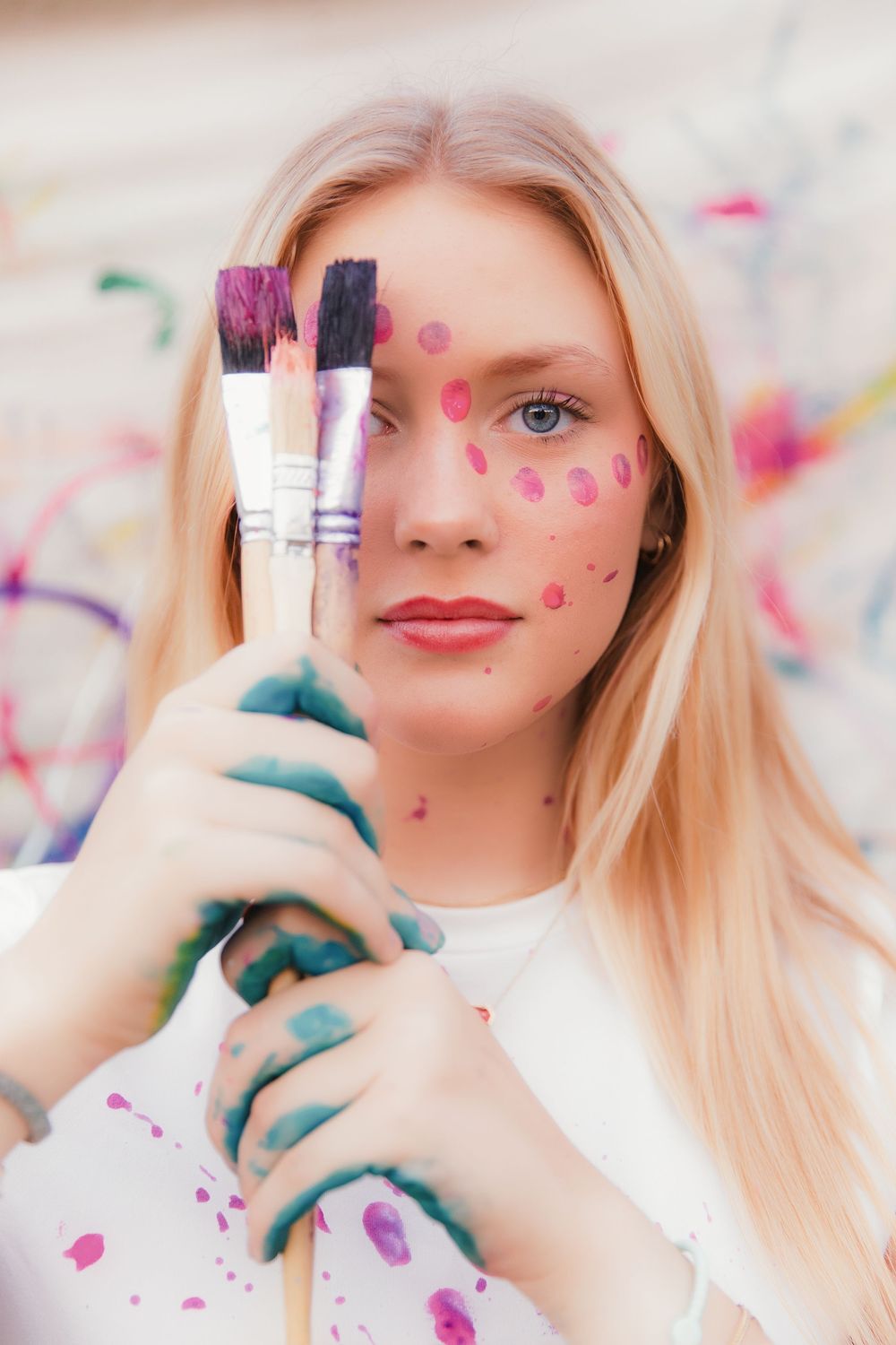 Creative portrait showing hands holding makeup brushes against a colorful confetti-decorated background.
