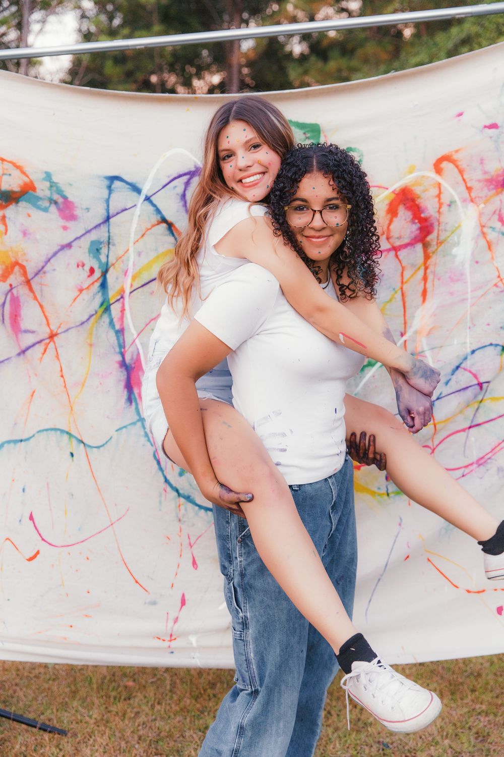 Two people pose playfully against a white backdrop with colorful paint splatters during a creative photoshoot.