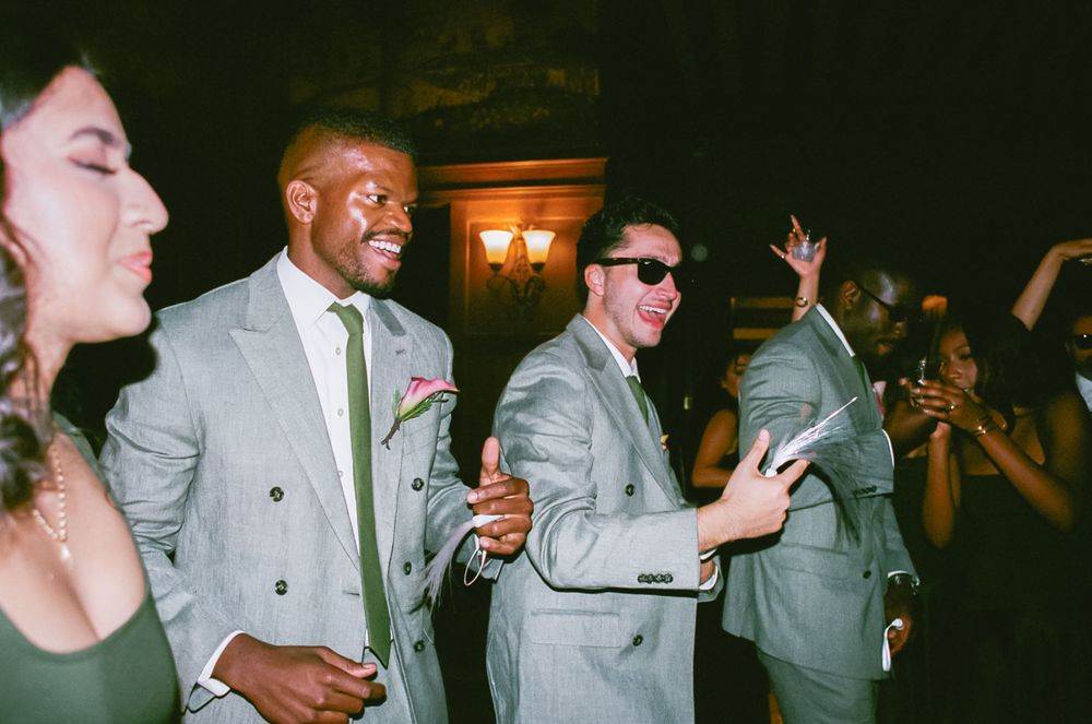 Party guests in formal attire dance and celebrate at an indoor event with warm lighting in the background.