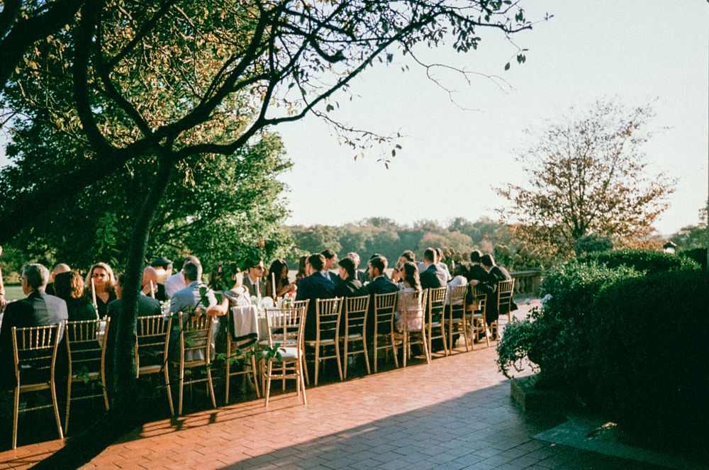 Rows of empty wooden chairs arranged outdoors at a wedding ceremony venue with trees in the background.