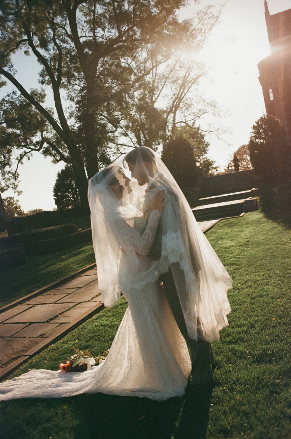 A bride in a flowing white wedding dress twirls gracefully on a grassy hill during golden hour sunset.