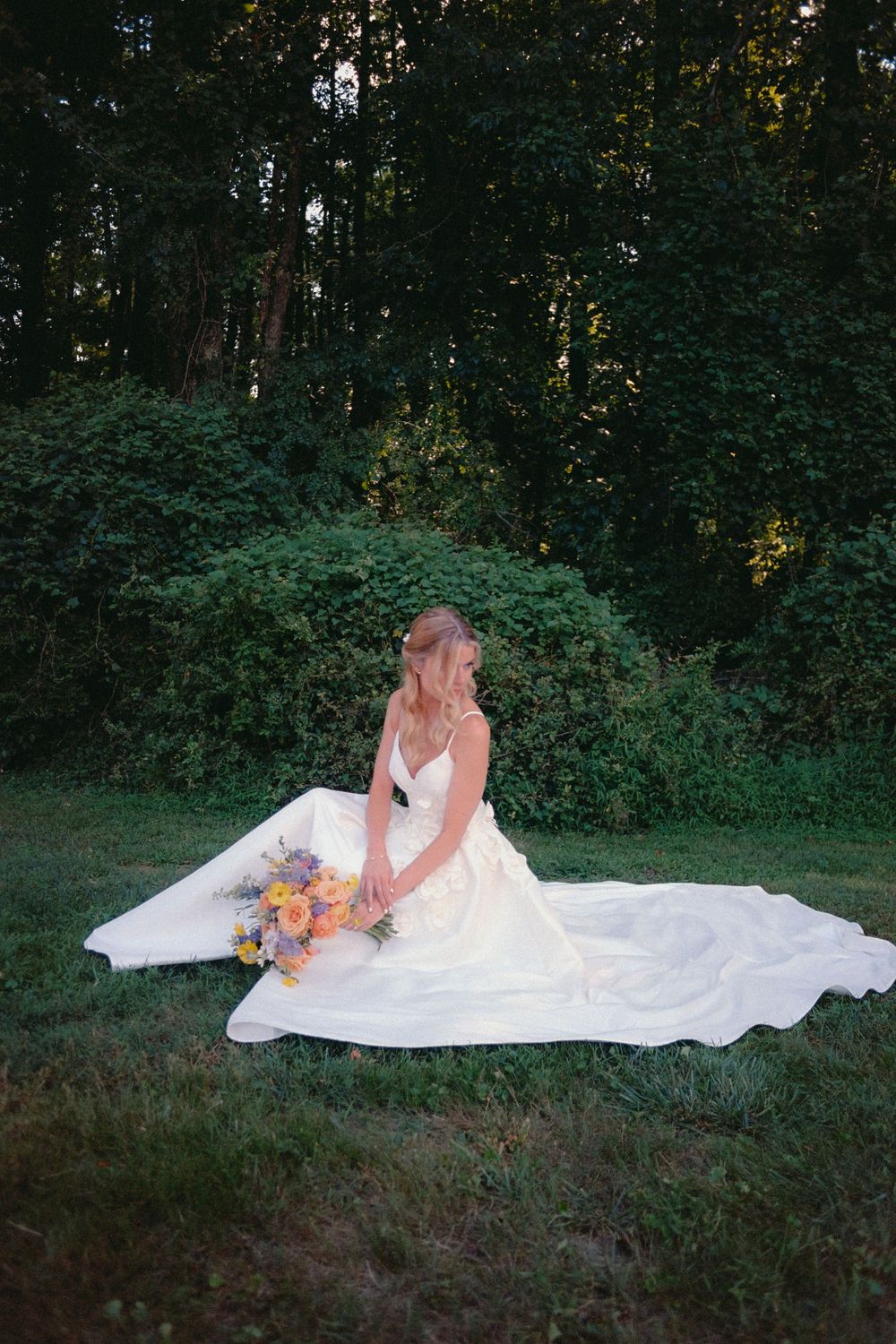 A bride in a flowing white dress poses on the ground for romantic outdoor portraits.
