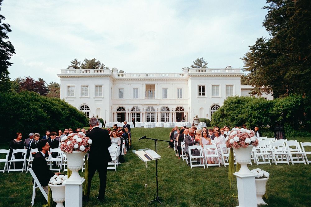 Outdoor wedding ceremony setup with white chairs arranged on a lawn in front of a grand white mansion.